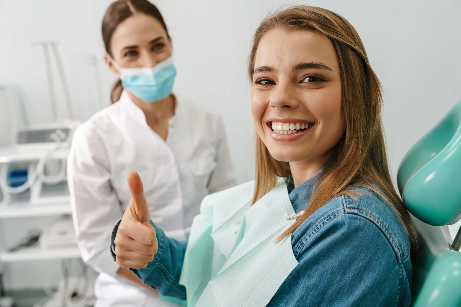 A smiling patient giving a thumbs up beside her dental hygienist